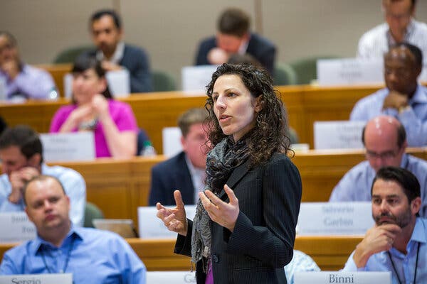 Francesca Gino, wearing a black blazer and dark scarf, speaking in a lecture hall filled with students.